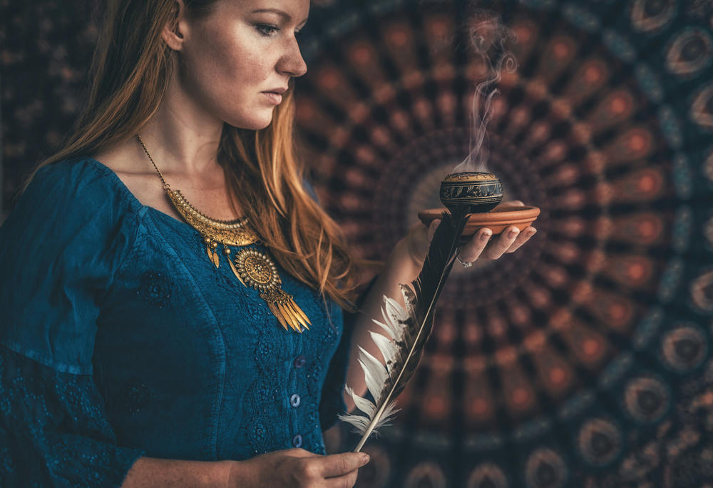  Incense in a woman's hand on a dark patterned background.