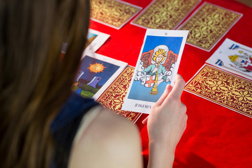 Fortune teller using tarot cards on a red table.