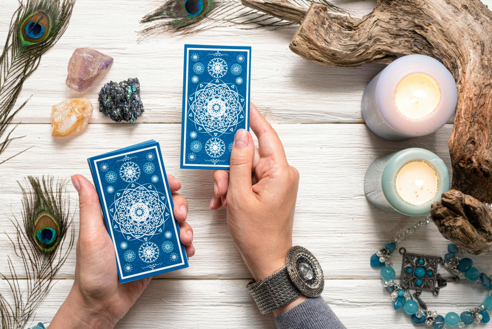 Fortune teller woman and blue tarot cards over white wooden table background.