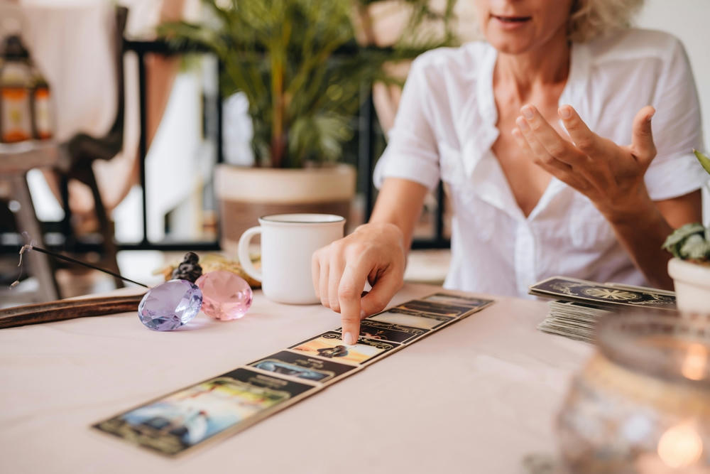 Mature professional tarologist having a session. A woman holding tarot cards and speaking with a customer about his life.