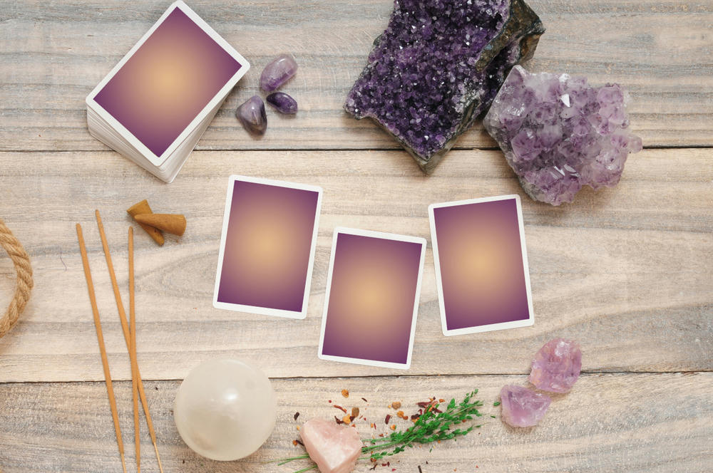 Tarot reading layout with wood background and crystals like amethyst and selenite, incense and dried plants.