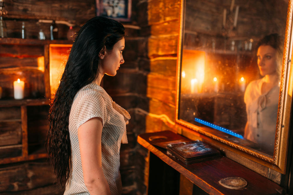 A young woman looking into the mirror practising a spiritual seance.