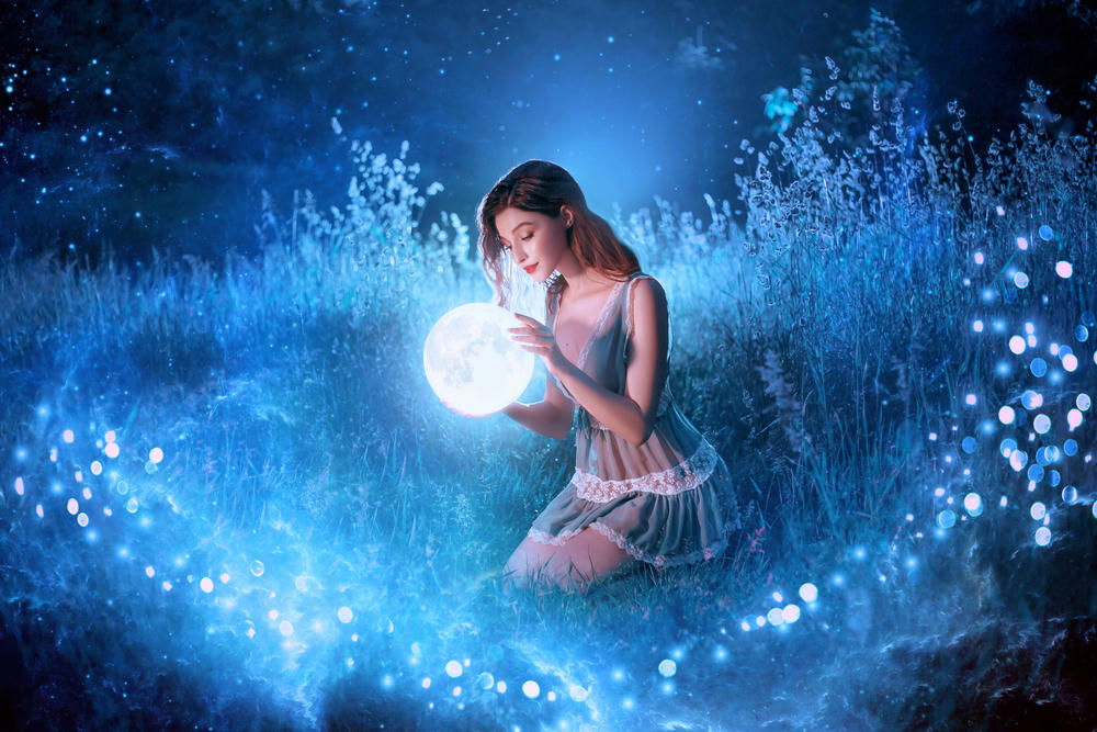 A young beautiful woman holds a magical ball at night in a dark forest.