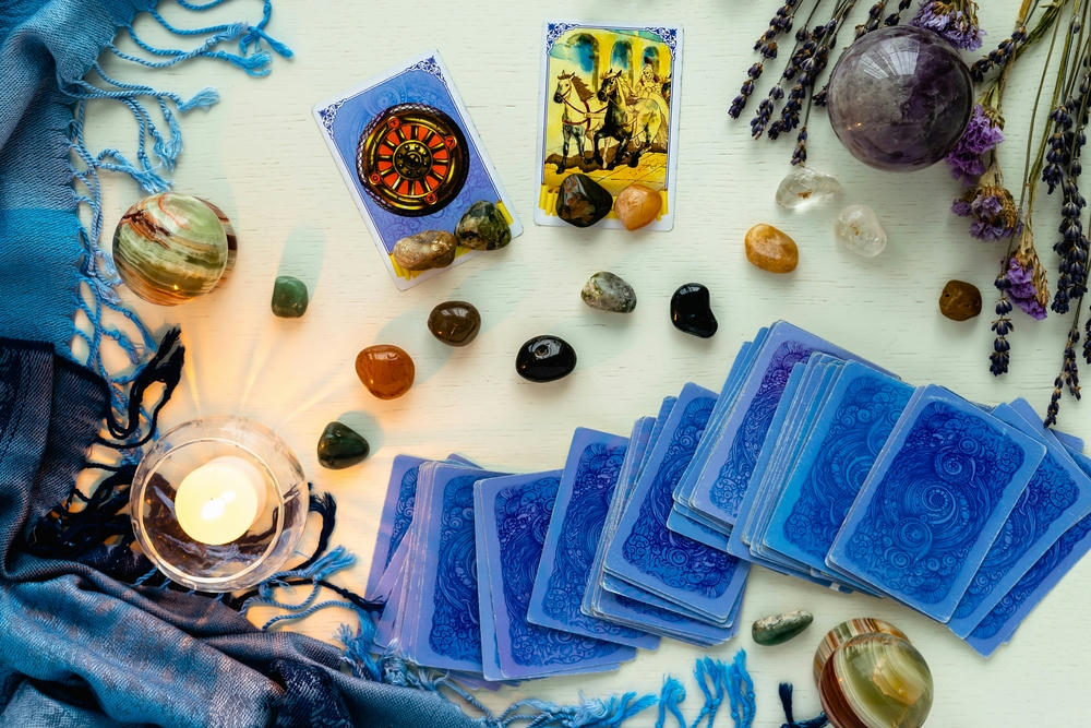 Fortune and chariot cards in tarot divination with candles and stones on a light table with dried flowers and a blue tablecloth.